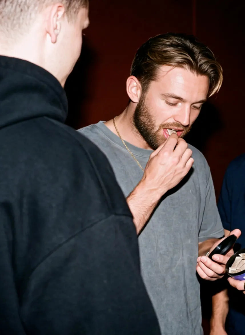 Young man putting a WAVE pouch under his lip at a party