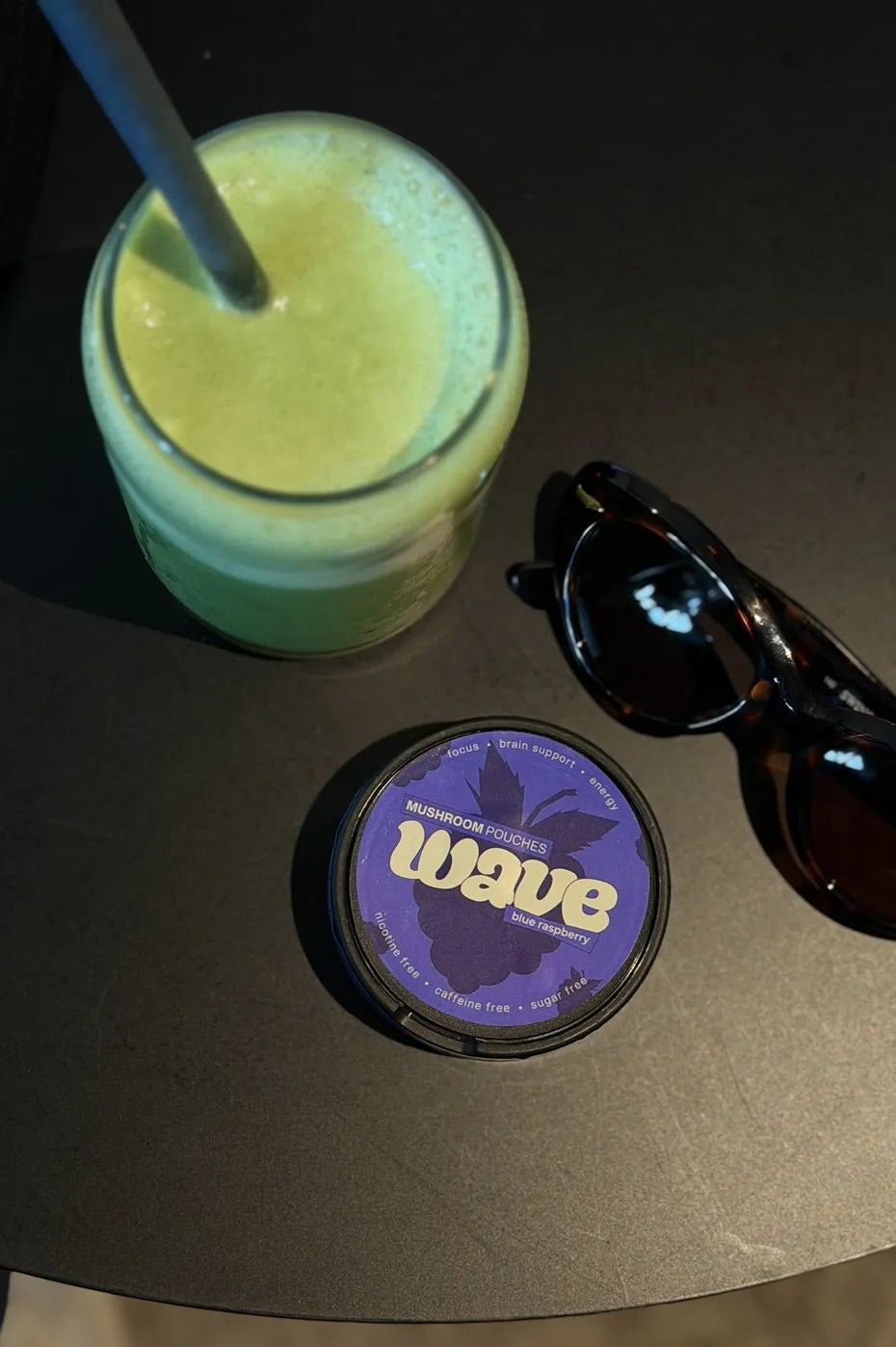 WAVE can on a dark table next to a green smoothie and sunglasses