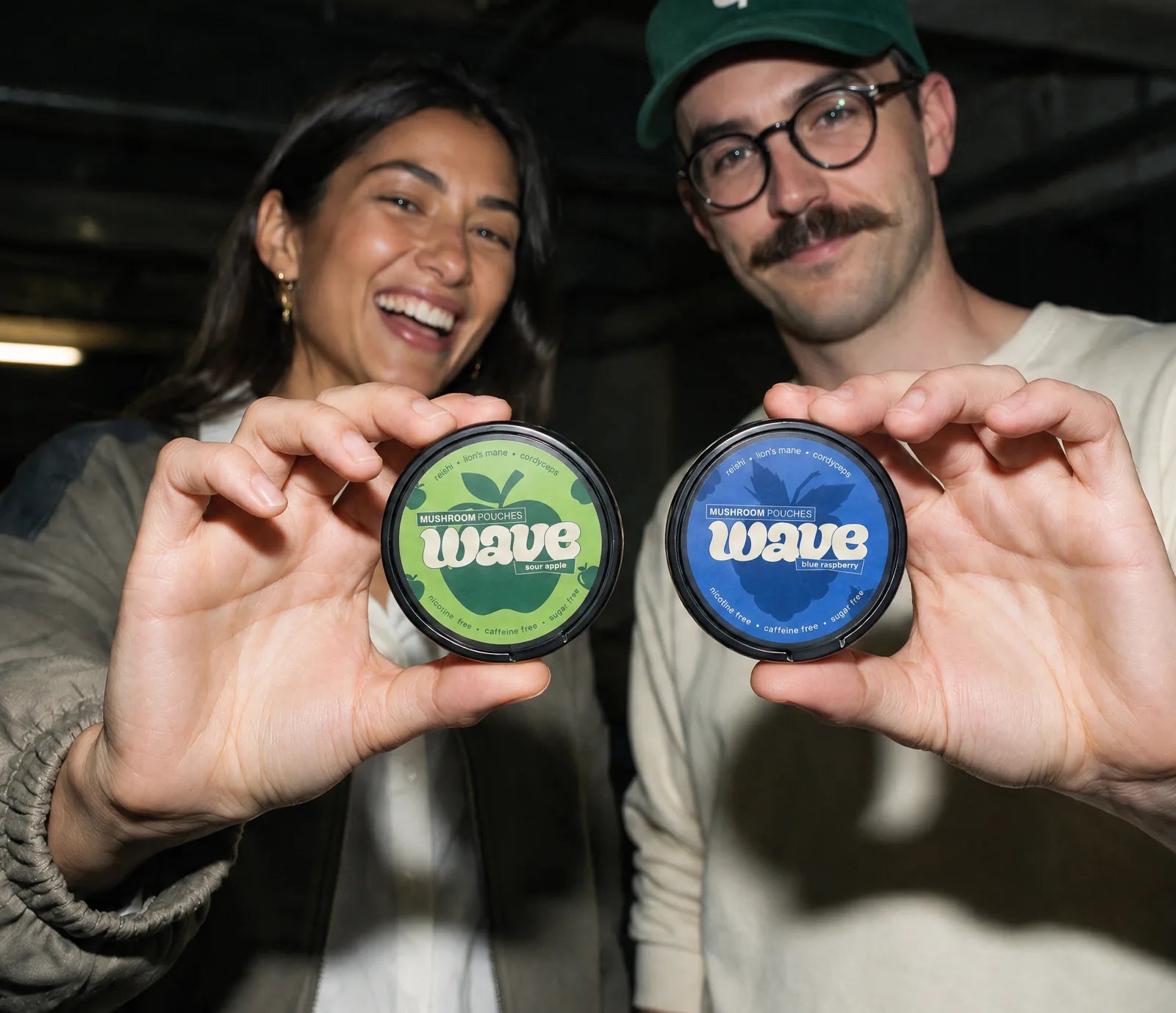 Deux amis dans un garage tiennent face à l’objectif une boîte WAVE Sour Apple et une boîte Blue Raspberry
