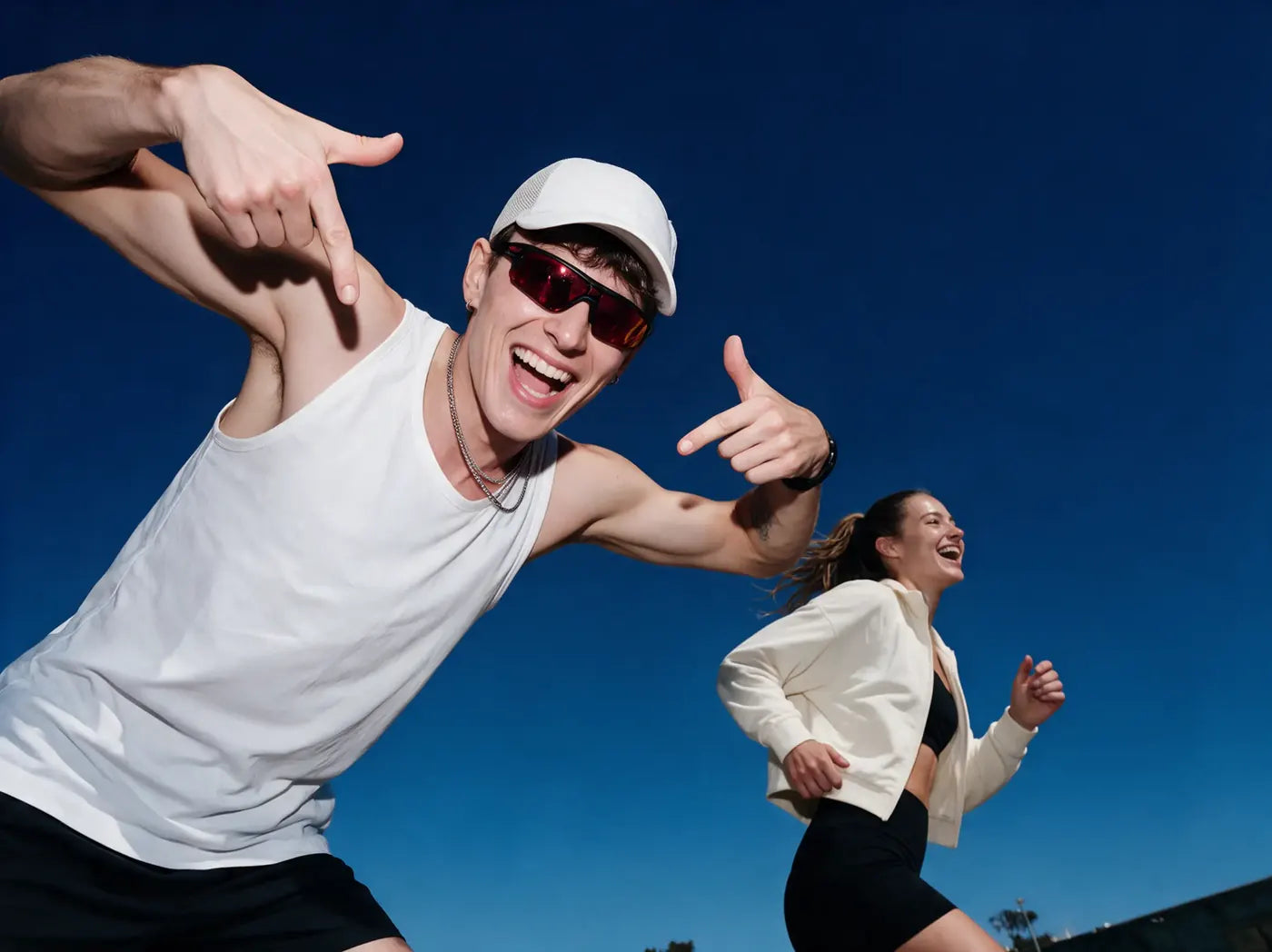 Un homme en casquette blanche rit tandis qu’une femme court derrière lui sous un ciel bleu