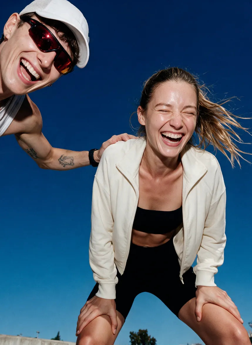 Two friends laughing outdoors under a clear blue sky